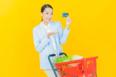 Renkli arka planda süpermarketten alınmış market sepetiyle gülümseyen güzel Asyalı kadın portresi.