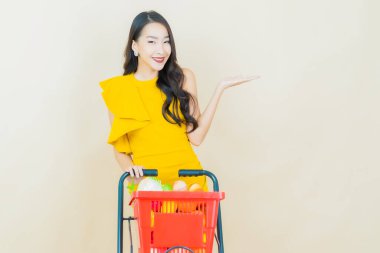 Renkli arka planda süpermarketten alınmış market sepetiyle gülümseyen güzel Asyalı kadın portresi.