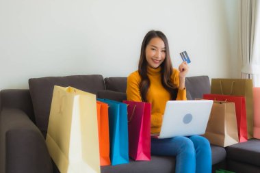 Genç Asyalı kadının oturma odasında online alışveriş yapmak için akıllı cep telefonu ve kredi kartı olan dizüstü bilgisayarı kullandığı portre.