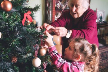 Genç bir kız ve büyükannesi Noel tatili için ağacı süslüyorlar. Aynı ailenin genç ve yaşlı kuşakları.
