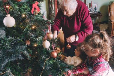 Genç bir erkek ve kız ve büyükanneleri Noel tatili için ağacı süslüyorlar. Aynı ailenin genç ve yaşlı nesilleri.