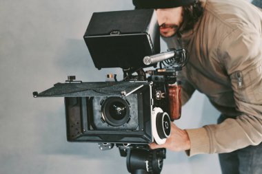 Sette çekim yapan bir film kamerasının arkasında genç bir erkek kameraman.