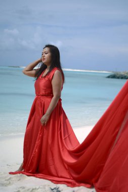 Lady in red satin flying dress flowing at the beach clipart