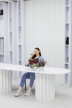 This photo shows a cosmetic dermatologist taking notes at her desk, surrounded by plants, books, and accessories. Her blue coat and professional focus convey a sense of clinical precision.