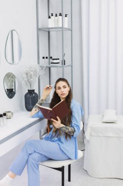 This photo shows a cosmetic dermatologist taking notes at her desk, surrounded by plants, books, and accessories. Her blue coat and professional focus convey a sense of clinical precision.