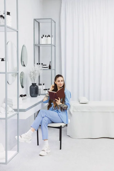 This photo shows a cosmetic dermatologist taking notes at her desk, surrounded by plants, books, and accessories. Her blue coat and professional focus convey a sense of clinical precision.