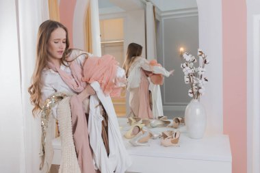 Pretty woman is looking for, sorting through, and trying on clothes in the wardrobe. Nothing To Wear concept. Fashion style. Shopaholic is upset.