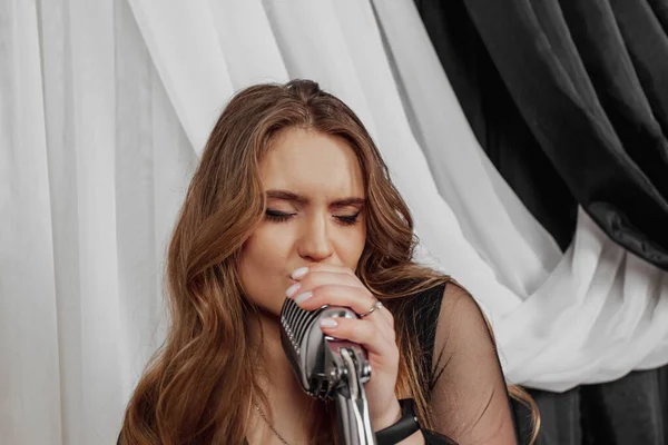 Elegant long haired brunette woman in black dress singing with the static microphone.