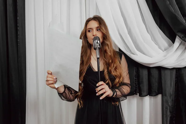 Elegant long haired brunette woman in black dress singing with the static microphone.