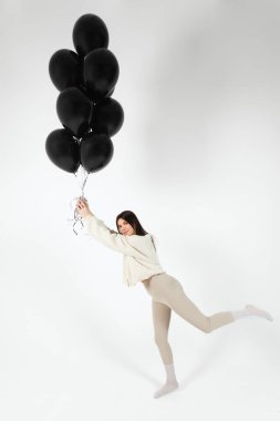 Brunette Girl in light clothes standing with a Bunch of black balloons and getting lifted up. Isolated on white background.
