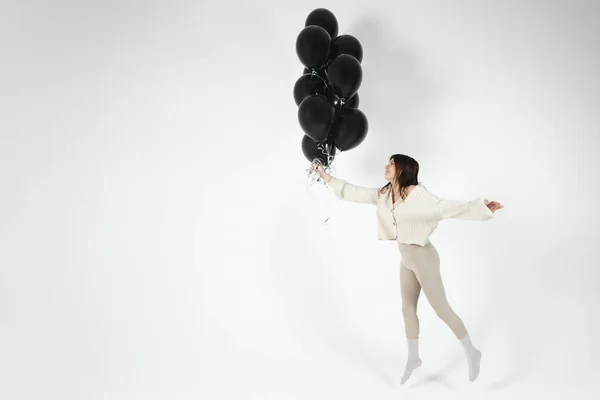 stock image Brunette Girl in light clothes jumping with Bunch of black balloons. Isolated on white background.