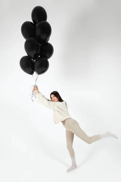 stock image Brunette Girl in light clothes standing with a Bunch of black balloons and getting lifted up. Isolated on white background.