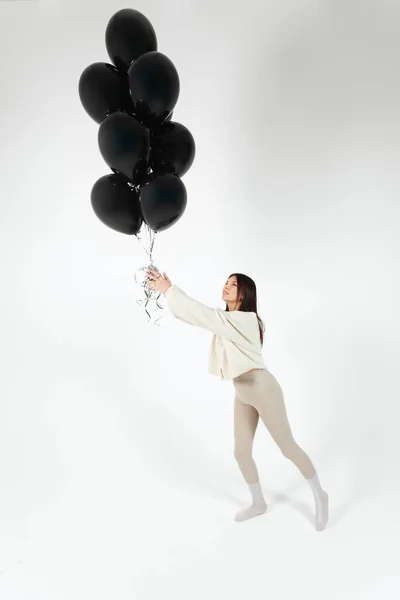 stock image Brunette Girl in light clothes standing with a Bunch of black balloons and getting lifted up. Isolated on white background.