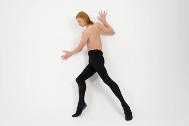 Young Athletic professional ballet dancer with a bare torso and black dance tights in a perfect shape performing over the white background.