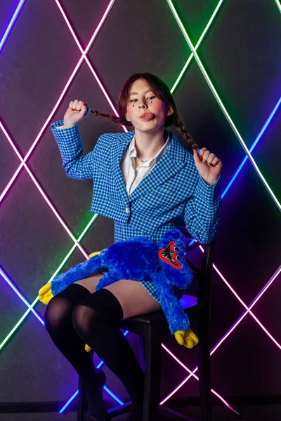 Portrait of a cute girl with drawn tears, dressed in a blue plaid jacket and skirt with knee high socks, sitting in a neon room pulling pigtails and showing tongue.