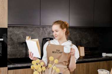 Bej önlüklü gülümseyen bir pasta şefi yemek tarifi kitabını okuyor. Boşluğu kopyala.