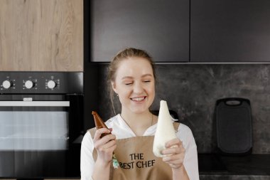 Bej önlüklü, gülümseyen bir pasta şefi elinde torba tutuyor ve pişirmeye hazır..