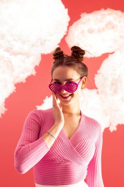 Pembe bluzlu ve kısa etekli çekici, parlak ve mutlu bir kız izole bir arkaplanda yüzen bulutlarla poz veriyor..