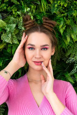 Taze yeşil yapraklı arka planda poz veren büyüleyici, parlak ve mutlu bir kızın portresi..