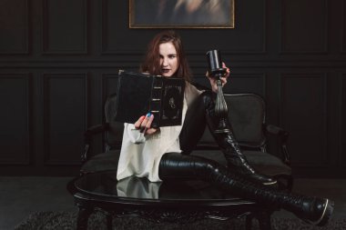 Mistik ya da büyülü bir kızın portresi gotik makyajlı ve kumral saçlı, açık beyaz gömlekli. Karanlık bir gotik odada elinde mum ve kitapla poz vermek..