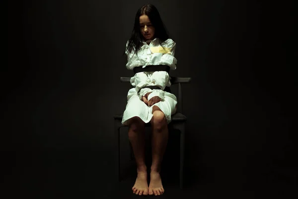 stock image A mentally unstable and ill woman in a straitjacket sitting in a chair in a psychiatric hospital on a black isolated background. Mental disorders concept. Crazy preson.