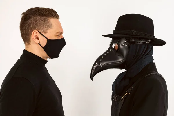 A Plague doctor and a man in a Medical mask looking at each other. a syringe and needle with Medicine or serum, antidote. Isolated on a white background. COVID-19, epidemic and pandemic concept.