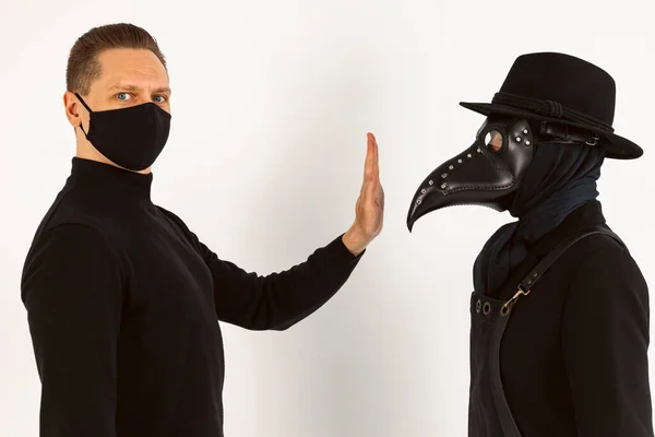 stock image A Plague doctor and a man in a Medical mask gestures not to approach. a syringe and needle with Medicine or serum, antidote. Isolated on a white background. COVID-19, epidemic,pandemic concept.