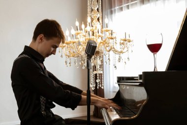 Siyah takım elbiseli, şık ve yakışıklı bir genç adam piyano çalıyor ve mikrofona şarkı söylüyor. yan görünüm.