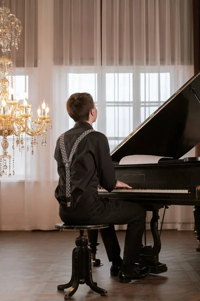 stock image Elegant, handsome young man in black suit and suspenders playing a piano. View from behind.