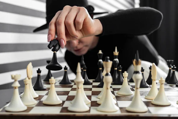 A girl in a black hat makes a move in chess. Close-up of a hand with the chess piece.