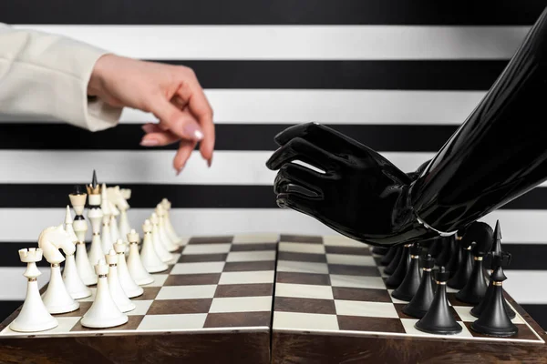 A chessboard, a human female hand, and an artificial robot hand. Playing chess with artificial intelligence, AI technologies, future.