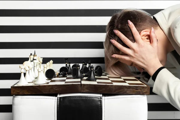 stock image An angry and upset woman gesticulates with her hands while sitting at a chessboard. Emotional defeat in the game.