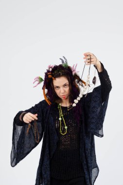 Siyah cüppeli ve boynuzlu bir kadın büyücü ya da şaman elinde tılsımlarla beyaz bir arka planda. Şamanik uygulamalar, ruhani ritüeller, Pagan inançları, doğaya ibadet, mistik.