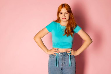 Hüzünlü kızıl saçlı genç bir kız soyutlanmış pembe bir arka plana karşı..