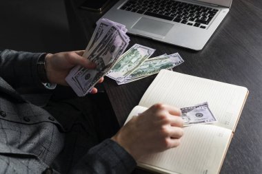 Gri takım elbiseli ve gözlüklü genç ciddi bir adam masasında oturup nakit sayıyor. Bir işadamı para tutar..