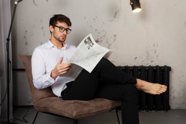 Elbiseli yakışıklı genç adam koltukta oturuyor ve endüstriyel tarzda gazete okuyor..