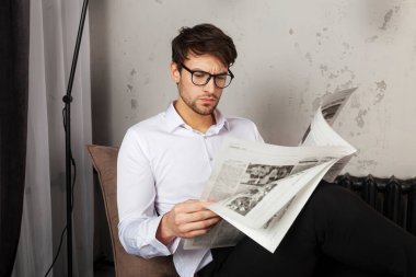 Elbiseli yakışıklı genç adam koltukta oturuyor ve endüstriyel tarzda gazete okuyor..