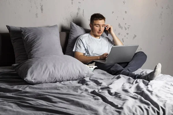 Jovem Trabalhando Casa Deitado Uma Cama Com Laptop Comida Falando — Fotografia de Stock