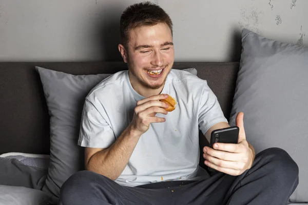 Jovem Está Sentado Cama Comendo Enquanto Fala Uma Chamada Vídeo — Fotografia de Stock