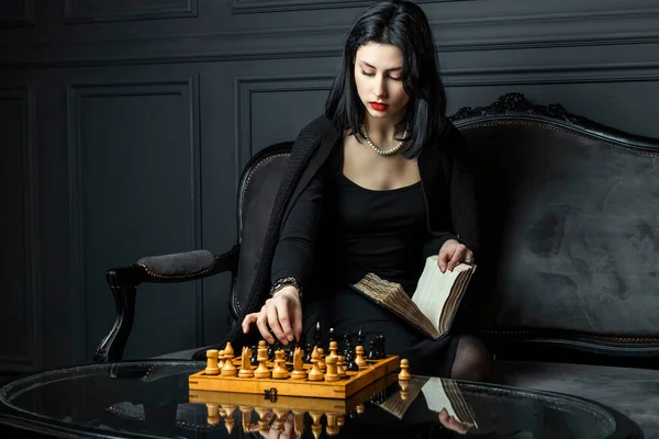 本と木製のチェス盤の後ろに座っている彼女の手と深刻です 彼女の顔に思慮深い表現 熱心に見つめて — ストック写真