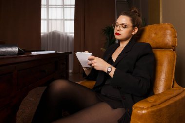 Güzel ve şehvetli bir psikolog, resmi giyinmiş ve çorap giyiyor, ofisinde oturuyor, elinde bir kalem ve defterle düşünüyor..