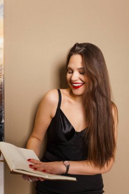 Uzun sarı saçlı zarif siyah elbiseli genç ve çekici bir kadın elinde kitapla gülüyor. Zevk ve keyif okuma kavramı.