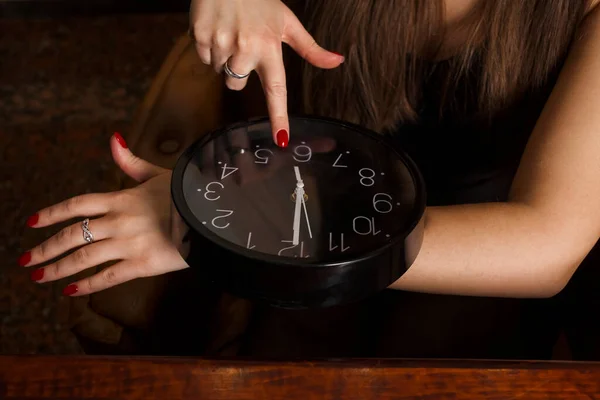 A young and attractive woman in an elegant black dress with long loose hair points to watch with her finger. Concept of punctuality and time management.