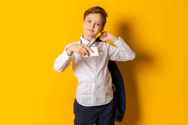 Beyaz gömlekli, kendine güveni tam küçük bir çocuk elinde mavi ceketi ve fotokopi alanı için beyaz bir rozeti var. Sarıda izole edilmiş..