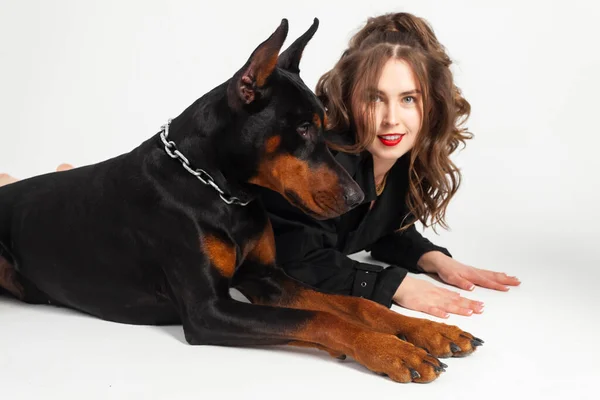 stock image A young beautiful Doberman with a chain around his neck and his owner, elegant girl in a long black coat and bright red lipstick. Isolated on a white background.
