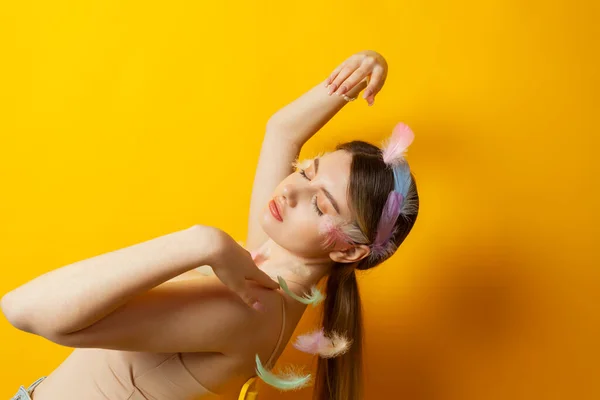 stock image Portrait of a lovely tender girl wearing feather decorations and corset top that almost blends with the color of her skin, posing. Isolated on a yellow background.