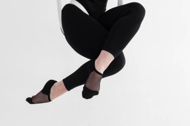 Siyah taytlı bir kadının bacaklarının, havadan ipeklerle veya kumaşlarla fiziksel ve zihinsel çabalar arasındaki dengeyi sağlayan ters dönmüş anti-yerçekimi hava yogası yaparken yakın plan çekimi. Beyazda izole edilmiş.