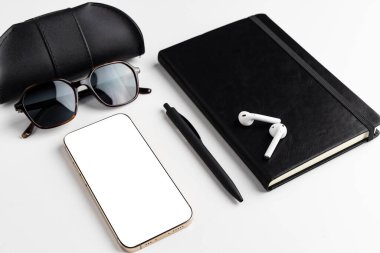 Siyah ve beyaz. Gözlük, güneş gözlüğü, kalem, kablosuz kulaklık, defter ve fotokopi alanı için boş beyaz ekranlı bir telefon için siyah deri çanta. Organizasyon ve verimlilik kavramı.