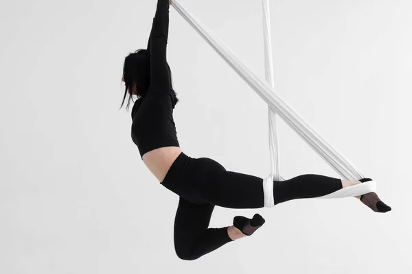 Female in black tights. Professional aerial performer. Inverted anti-gravity Aerial yoga with the use of aerial silks or fabrics, Balance between physical and mental effort concept. Isolated on white.