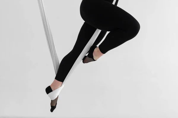 Close-up of a woman\'s legs in black tights performing an Inverted anti-gravity Aerial yoga with the use of aerial silks or fabrics, Balance between physical and mental effort. Isolated on white.